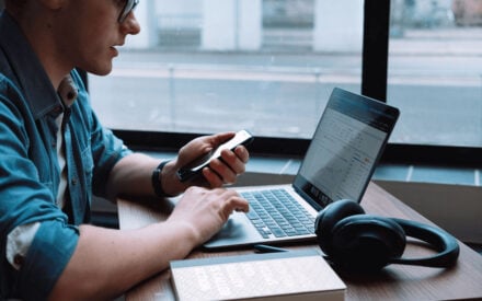 Germans Frolovs analyzing data on a laptop while using a phone