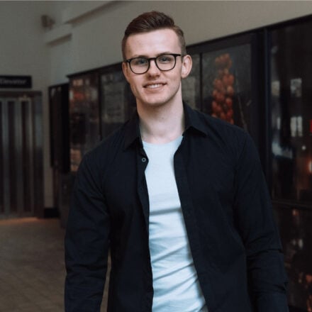 Germans Frolovs smiling in business casual attire in a modern hallway