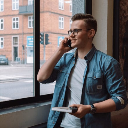 Germans Frolovs smiling while talking on the phone by a window holding a notebook