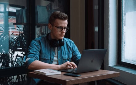 Germans Frolovs working on a MacBook with headphones around his neck in a cafe