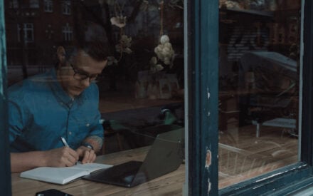 Germans Frolovs writing in a notebook next to a laptop in a cafe
